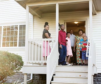 Yohani, Vestine, and their five children stand on the porch of their first home which they purchased after graduating from Emmanuel House